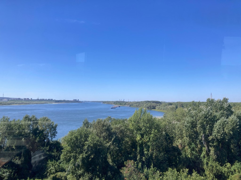 A panoramic view of a river surrounded by lush greenery under a clear blue sky.